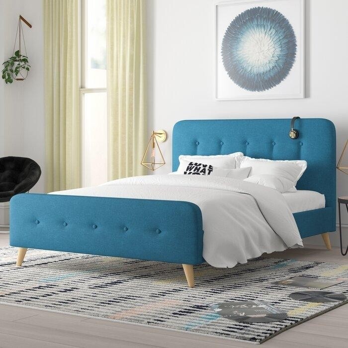 мягкая темно-бирюзовая кровать на светлых ножках, современная геометрическая бра и серо-голубая картина над кроватью.jpeg