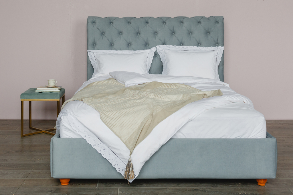 спальня с серо-голубой мягкой кроватью с оранжевыми ножками и мягким пуфиком вместо прикроватной тумбочки