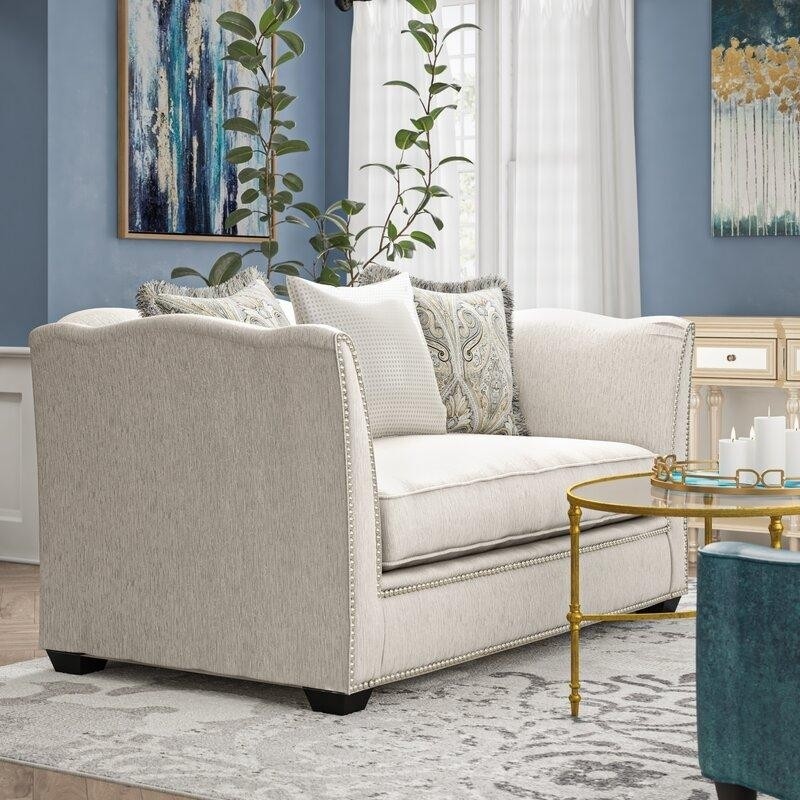 элегантный светлый двухместный диванчик с отделкой декоративными гвоздиками в серо-голубой гостиной с журнальным столиком на металлических ножках золотого цвета и стеклянной столешницей.jpeg
